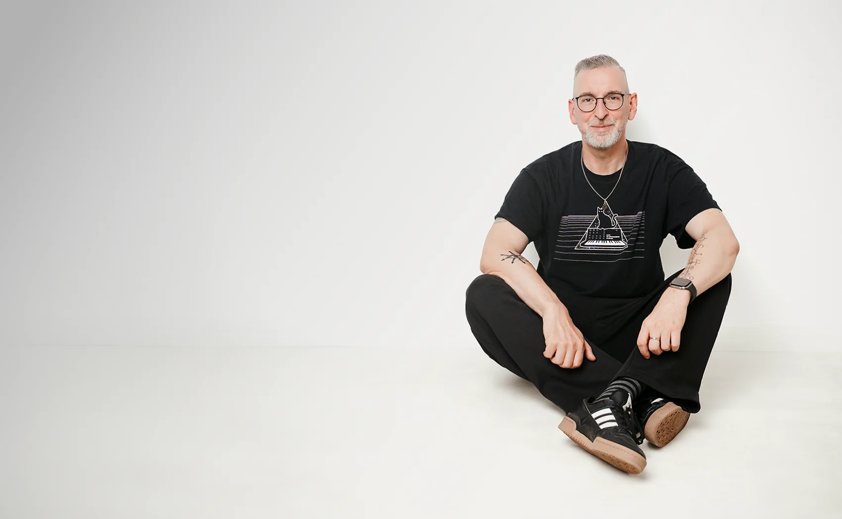 Michael Kißing sitzt entspannt auf dem Boden, mit Brille und im schwarzen T-Shirt